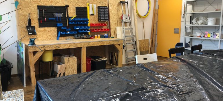 Man sieht eine Werkbank auf Holz, welche mit verschiedenen Werkzeugen und Abreitsmaterial, wie Schrauben Nägel etc. bestückt ist. 