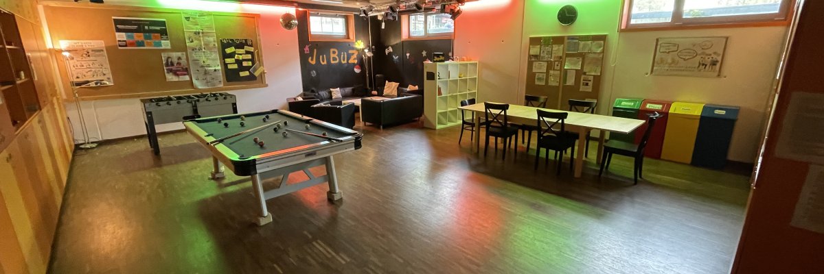 Bildbeschreibung: Blick in den Jugendraum. Man sieht einen großen Tisch, einen Billiard-Tisch und einen Kicker. Daneben eine Sitzgruppe. Es wirkt sehr gemütlich.