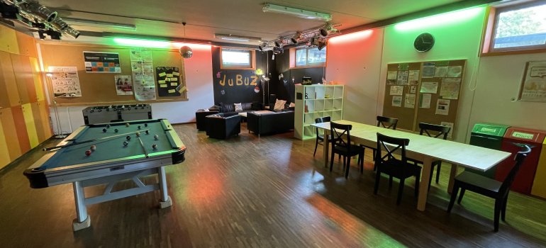 Bildbeschreibung: Blick in den Jugendraum. Man sieht einen großen Tisch, einen Billiard-Tisch und einen Kicker. Daneben eine Sitzgruppe. Es wirkt sehr gemütlich.