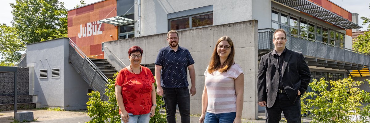 Bildbeschreibung: Zwei Frauen und zwei Männer stehen auf Steinen in frühlingshaftem Ambiente und lächeln in die Kamera. Das Team des JuBüZ ist zu sehen. Im Hintergrund ist auch das Haus erkenntlich.