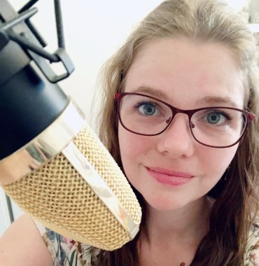 Bildbeschreibung: Junge Frau mit roter Brille, im Vordergrund ein Mikrofon